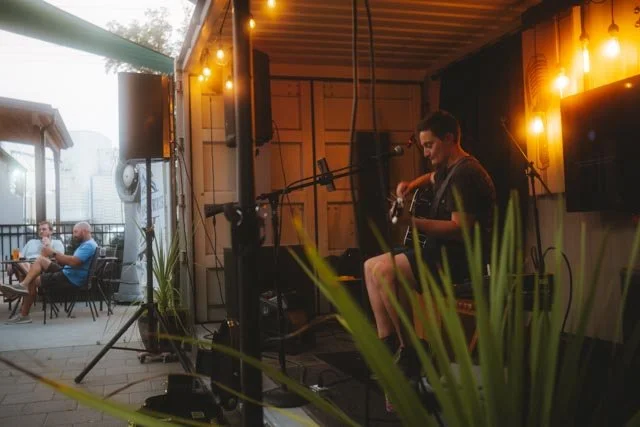 An outdoor live-music performance with guests seated nearby and warm venue lighting