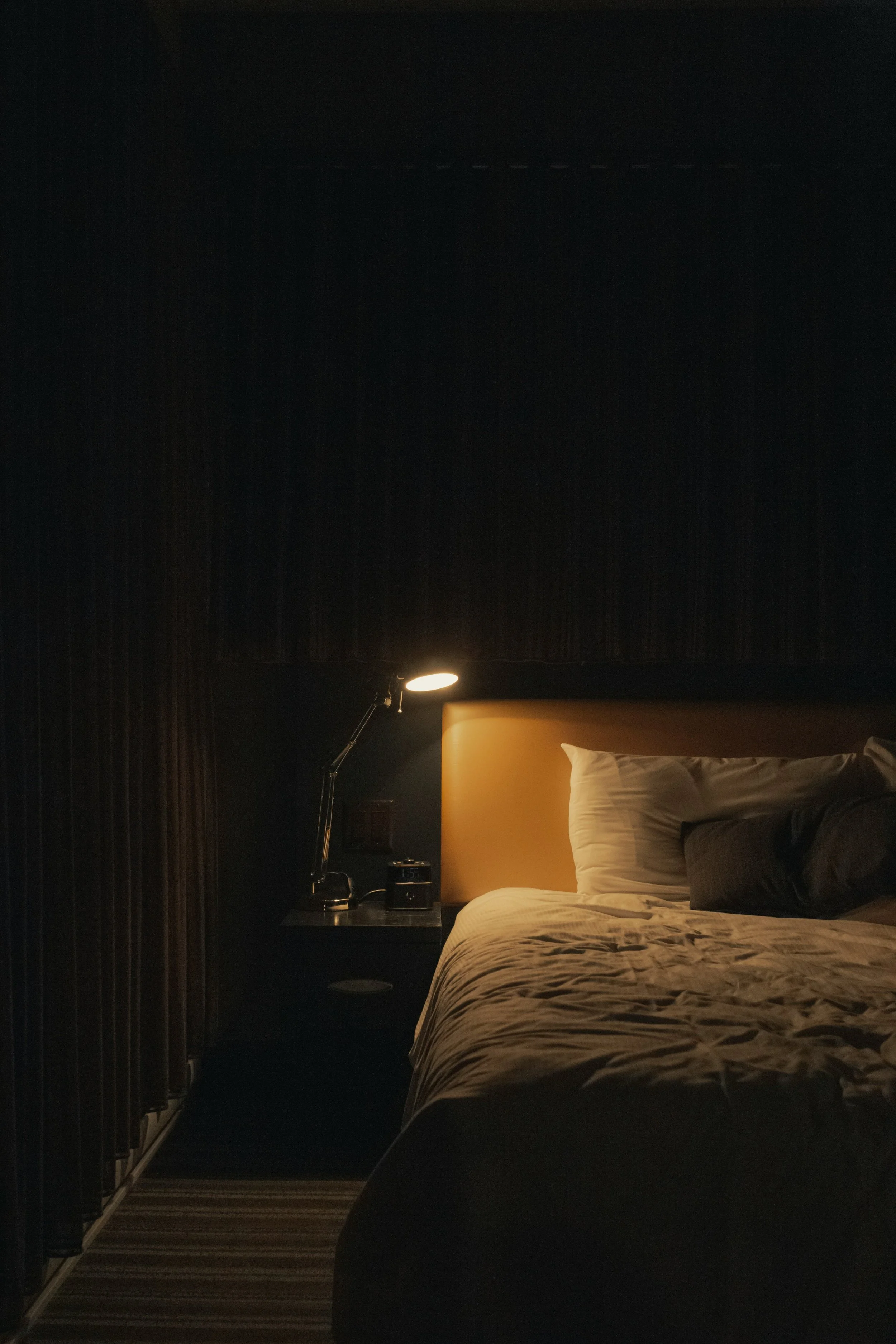 Bedside lamp glowing beside a bed in a dark bedroom at night