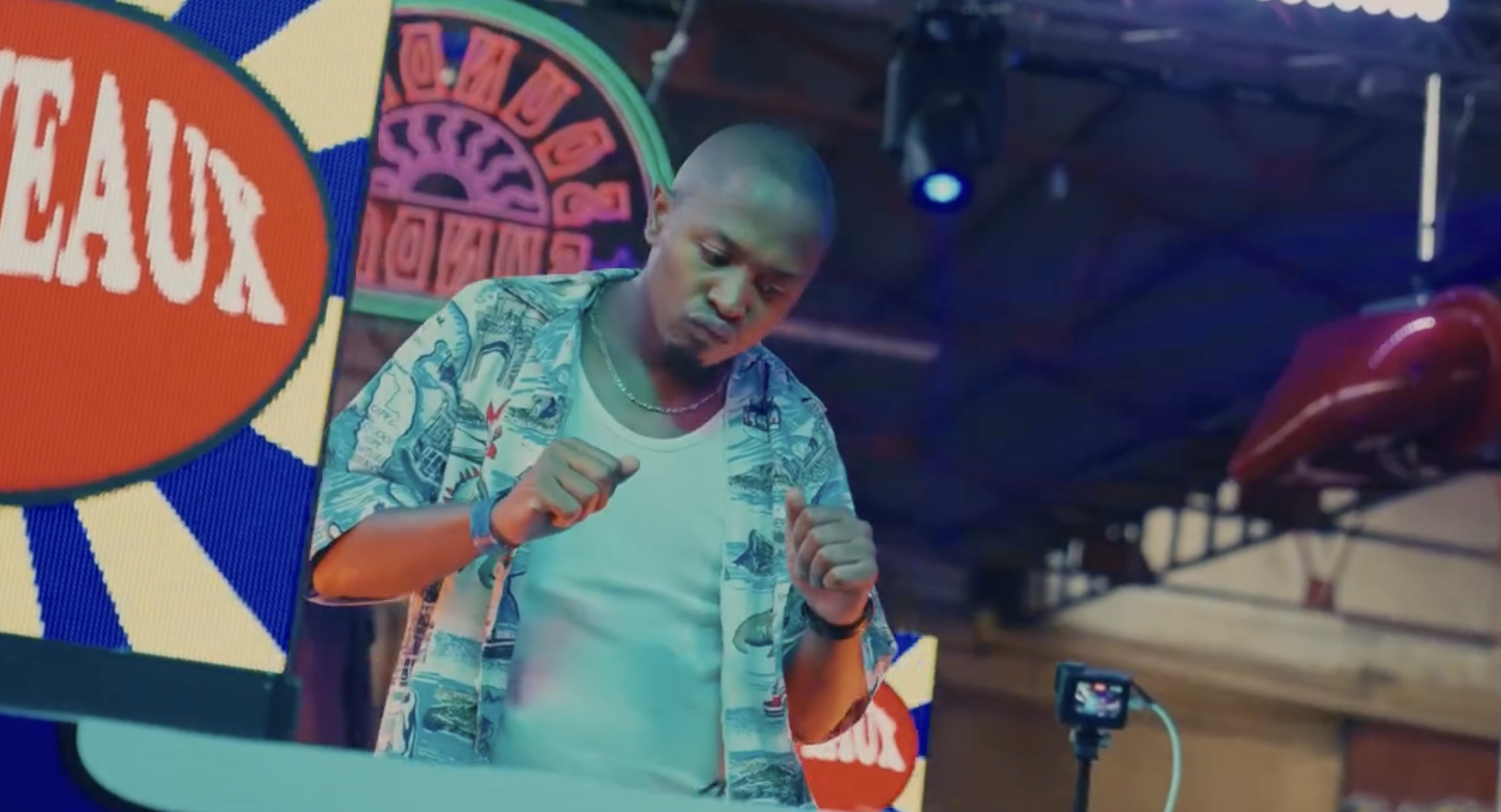 A young man with a shaved head dancing or moving with his fists raised in front of a colorful LED screen at a nightclub or party.