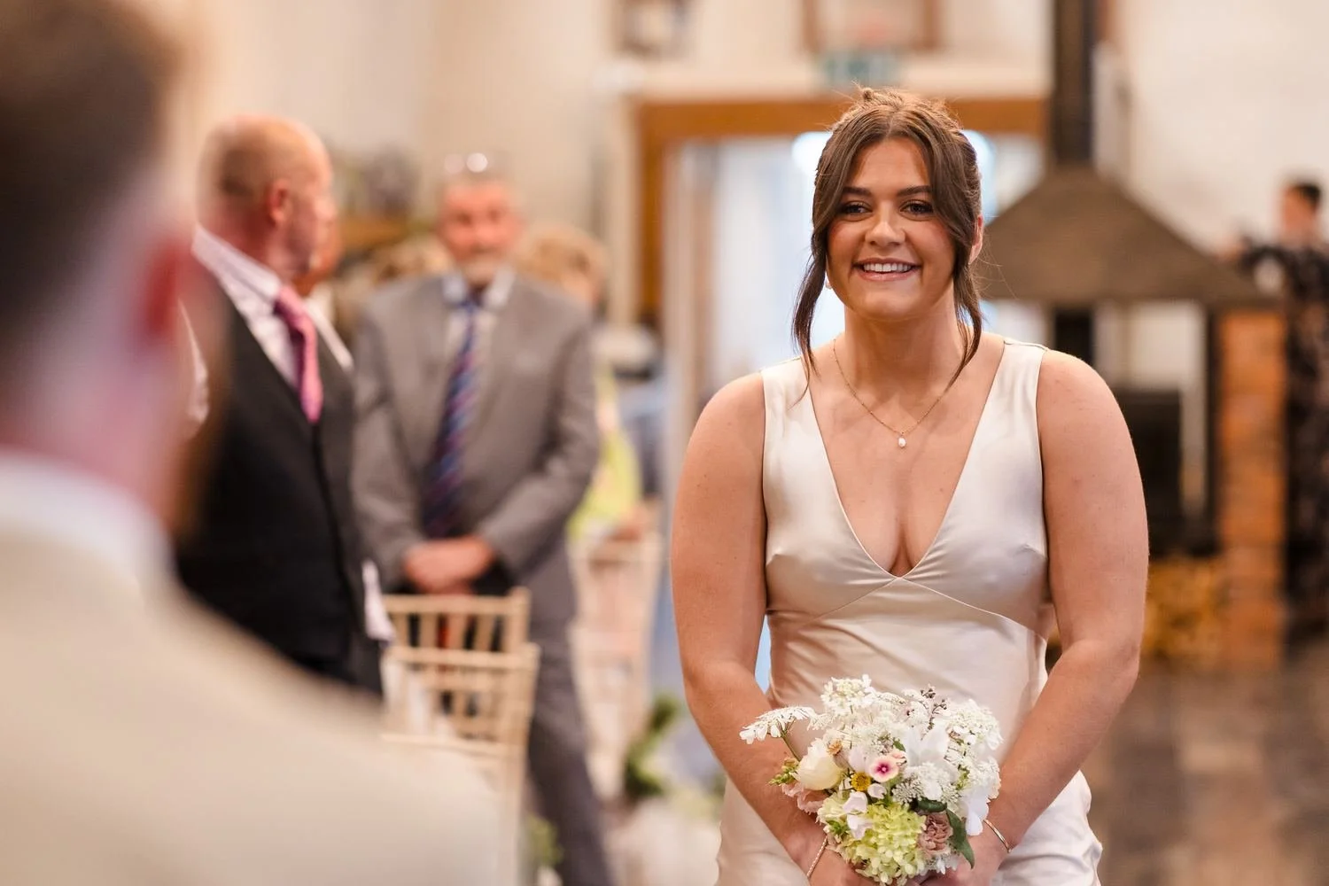 Smiling bridesmaid in a champagne satin dress walking down the aisle in the barn at Bennetts Willow Barn