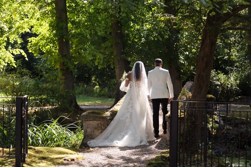 Bride and groom walking away hand in hand across the moss-covered stone bridge at Hogarths Hotel Solihull.