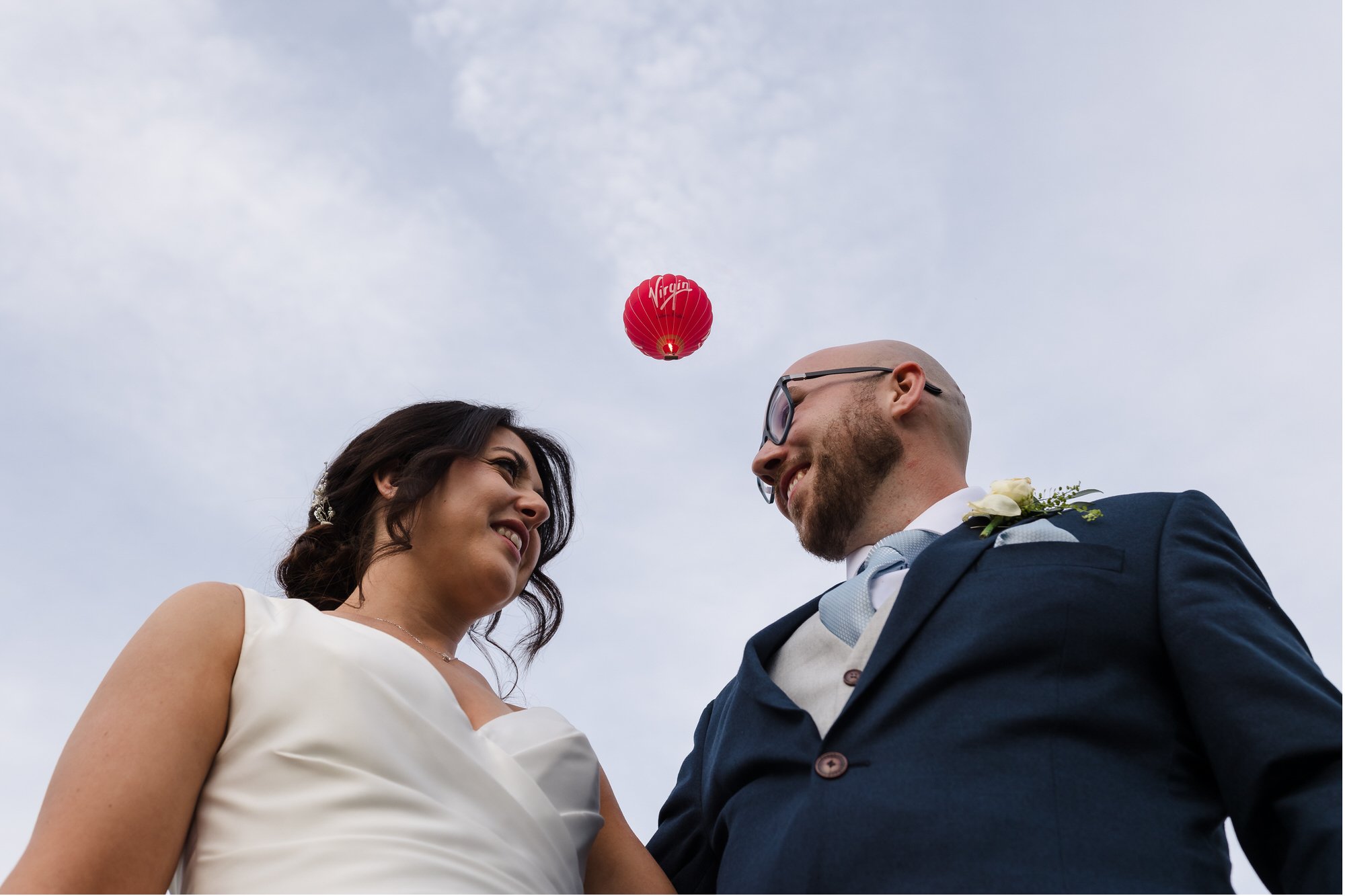 Bride and groom laughing as they watch a small red balloon rise into the sky at their Worcestershire wedding