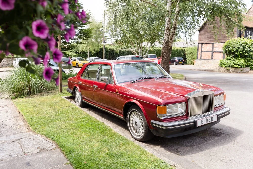 Vintage red Rolls-Royce parked by flowers and birch trees on the grounds of Karma Salford Hall.