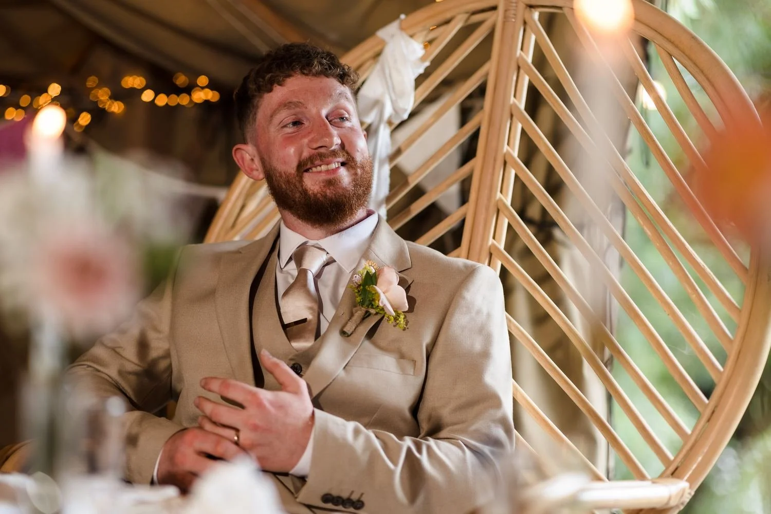 Sean smiling at the top table in a rattan peacock chair as he listens to the speeches