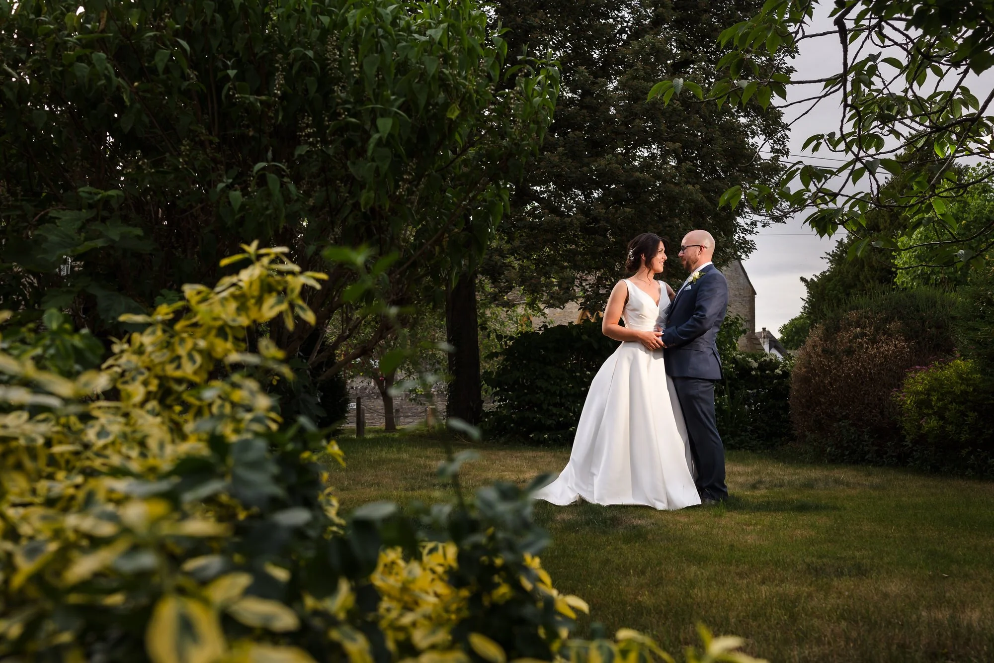 Bride and groom embracing beneath trees in a walled garden, natural light couple portrait at a Worcestershire wedding