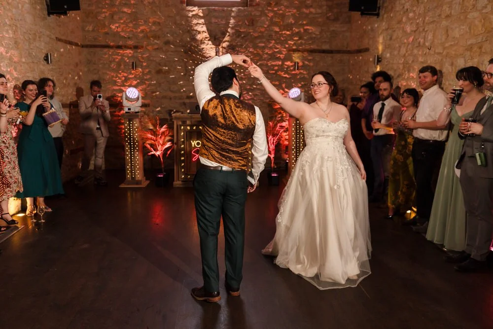 Bride and groom's first dance inside the barn at Huntsmill Farm, guests watching under red uplighting.