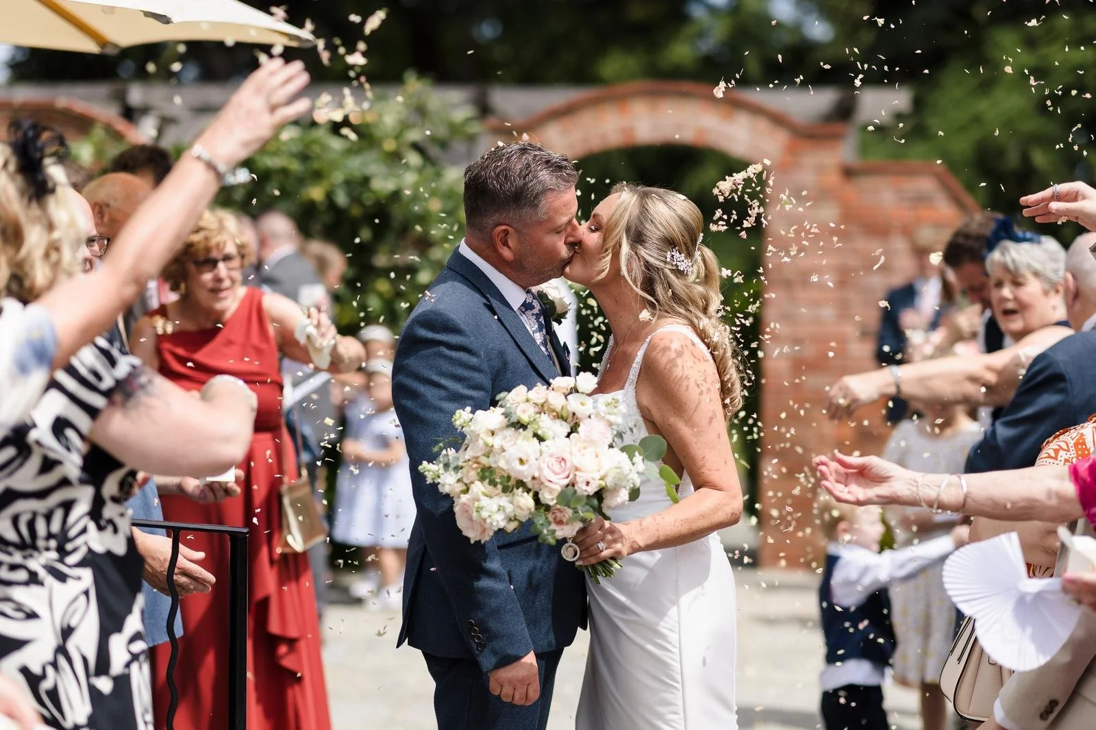 Charlotte and Richard's confetti walk through Ashton Lodge's brick archway wedding photography by Once in a Lifetime Photography