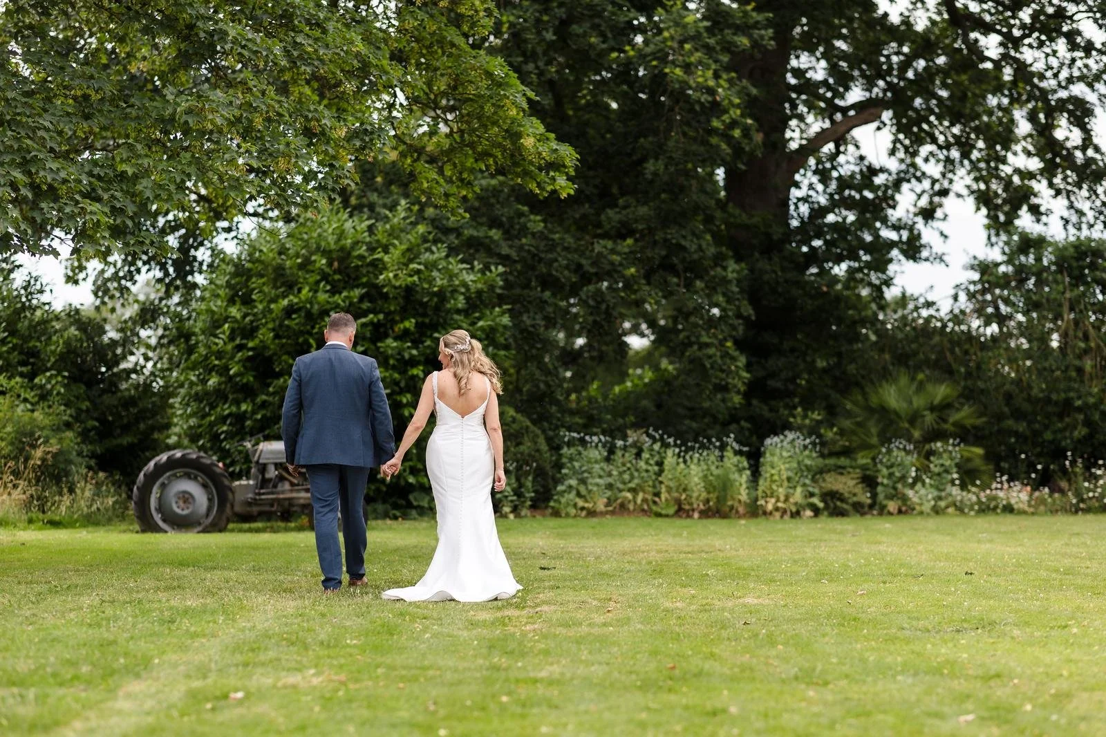 Newlyweds walking hand in hand past an old tractor at Ashton Lodge Country House wedding photography by Once in a Lifetime Photography