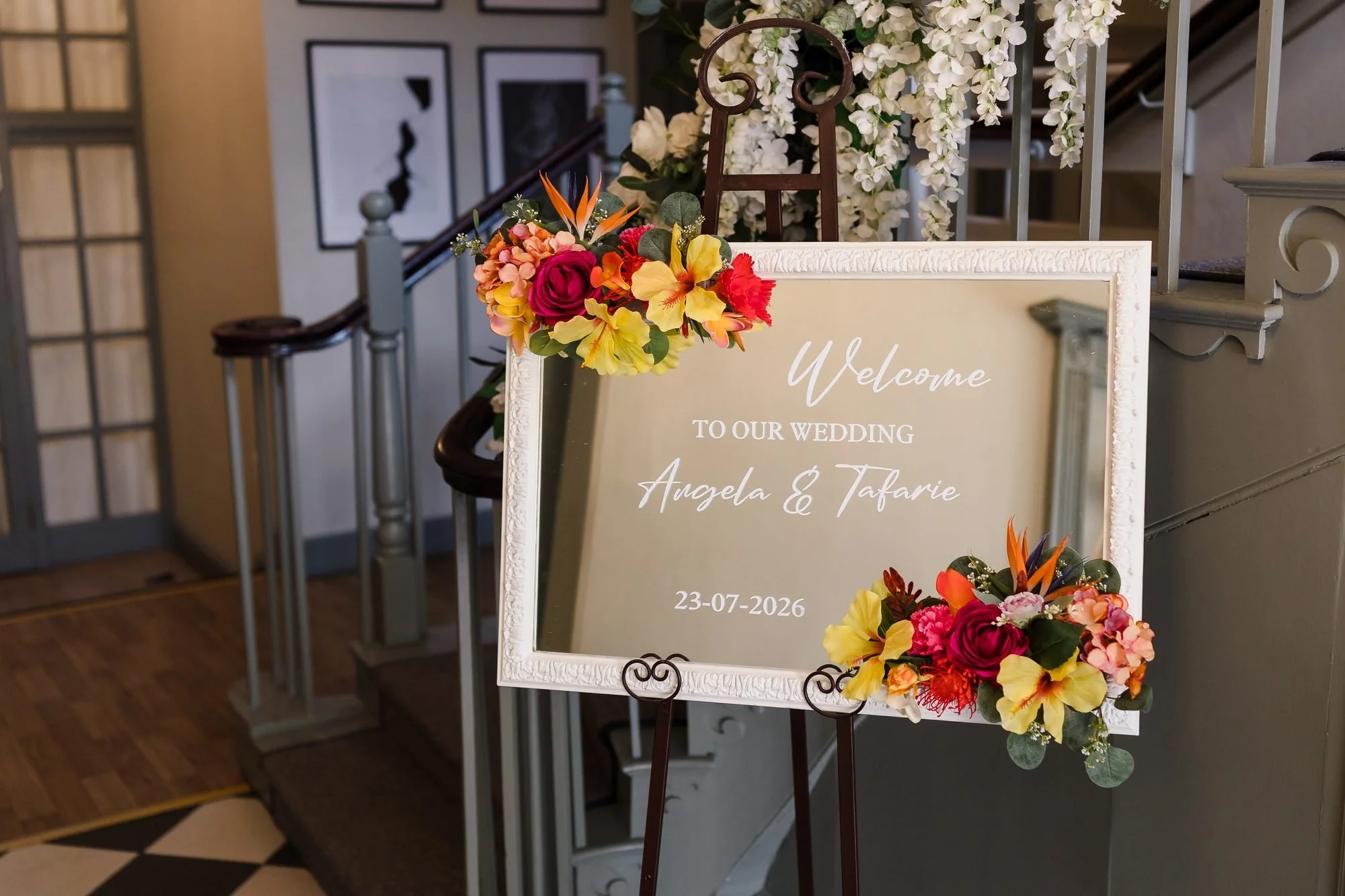 Angela and Tafarie's wedding welcome sign with tropical flowers beside the staircase at Warwick House