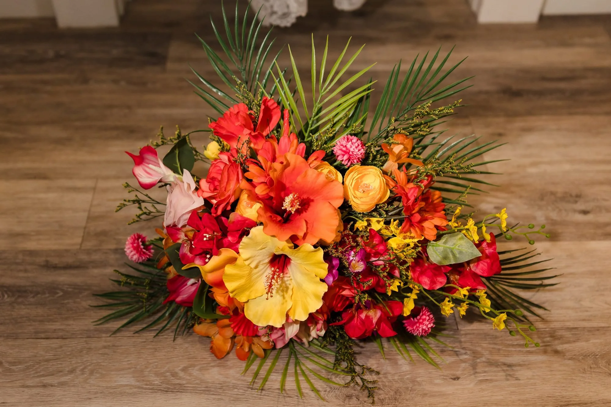 Bright tropical bridal bouquet of hibiscus, roses and palm leaves on a wooden floor at Warwick House