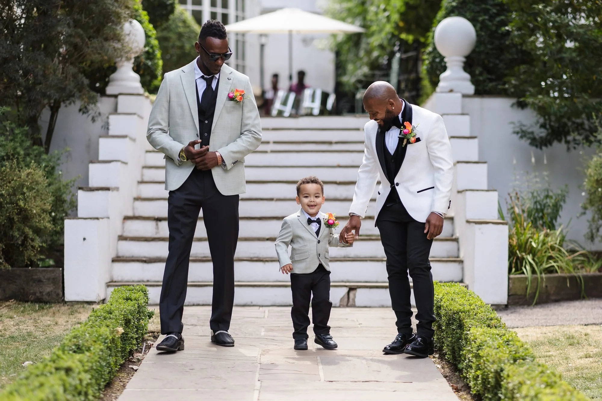 Groom holding his young son's hand as they walk down the garden steps to the outdoor ceremony at Warwick House