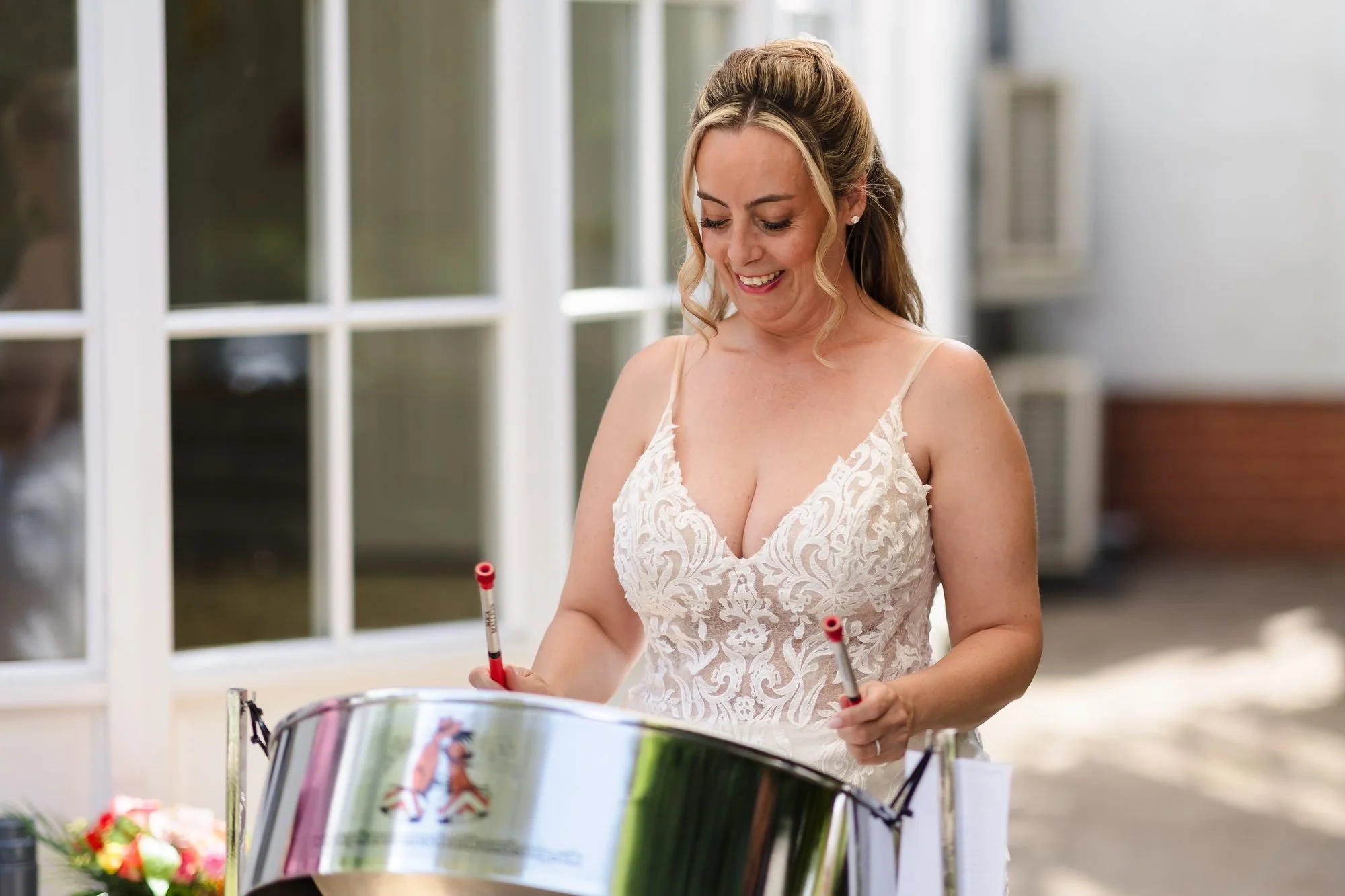 Bride Angela laughing as she tries the steel pans during her drinks reception at Warwick House