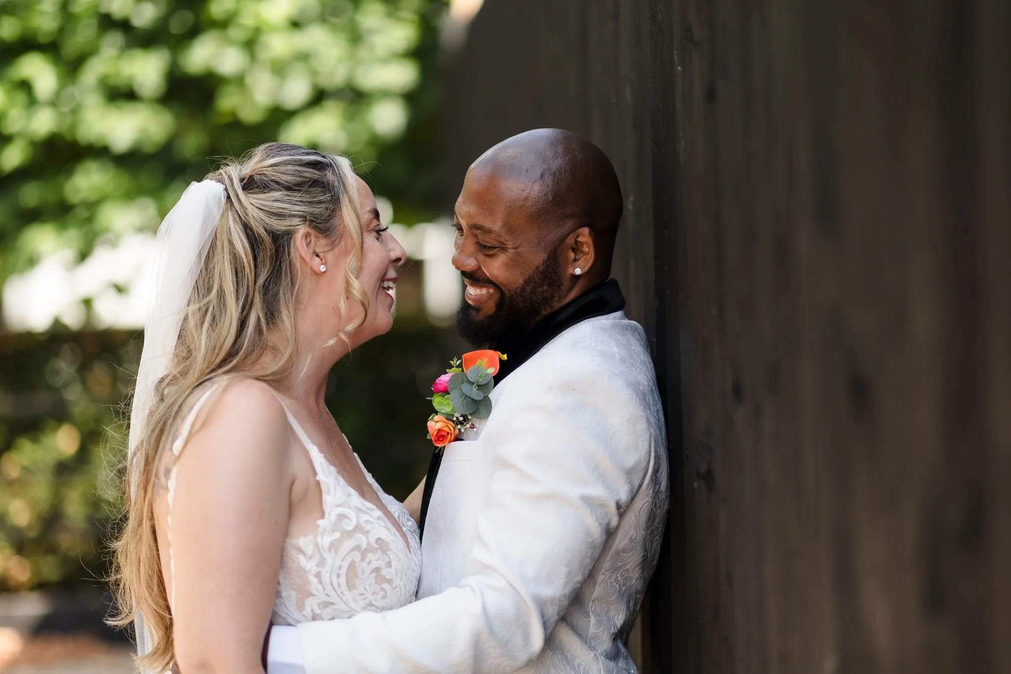 Bride and groom sharing a laugh in a close embrace against a dark wooden wall at Warwick House