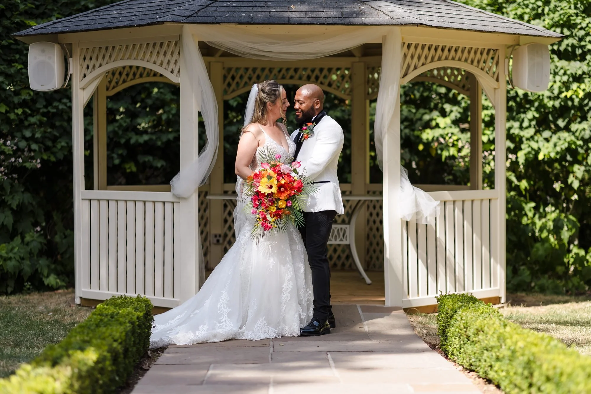 Bride and groom standing close together in the white garden gazebo at Warwick House in summer sunshine