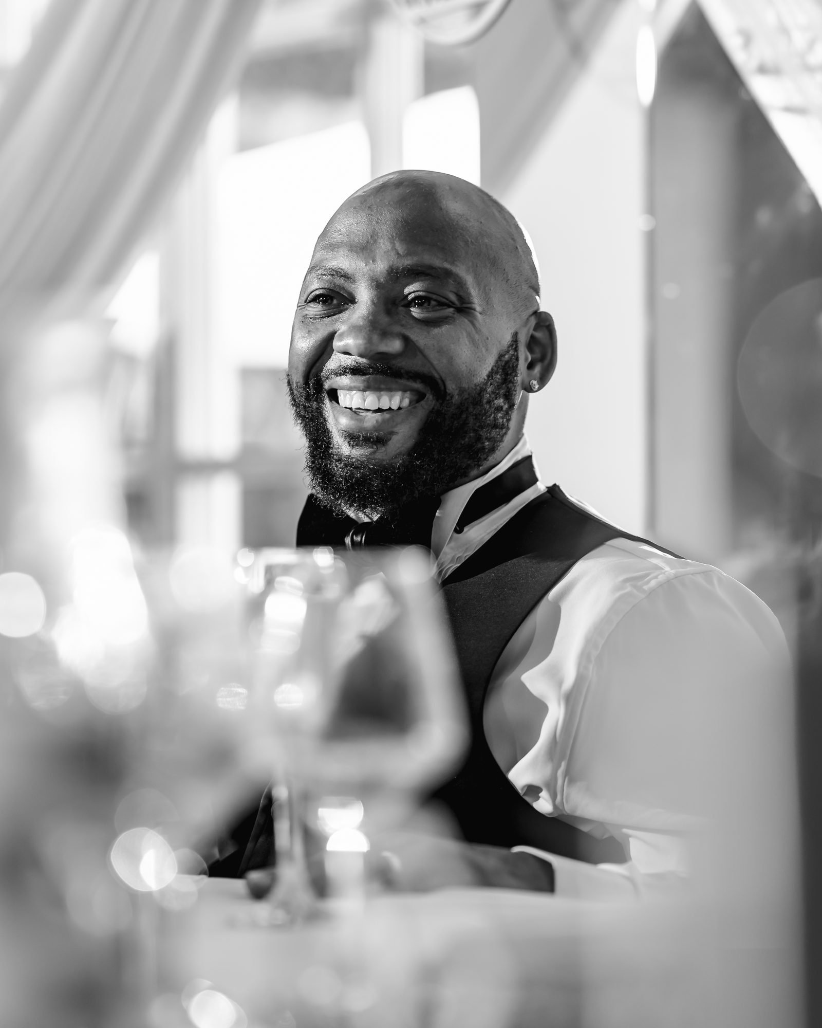 Black and white photo of the groom laughing during the wedding speeches at Warwick House