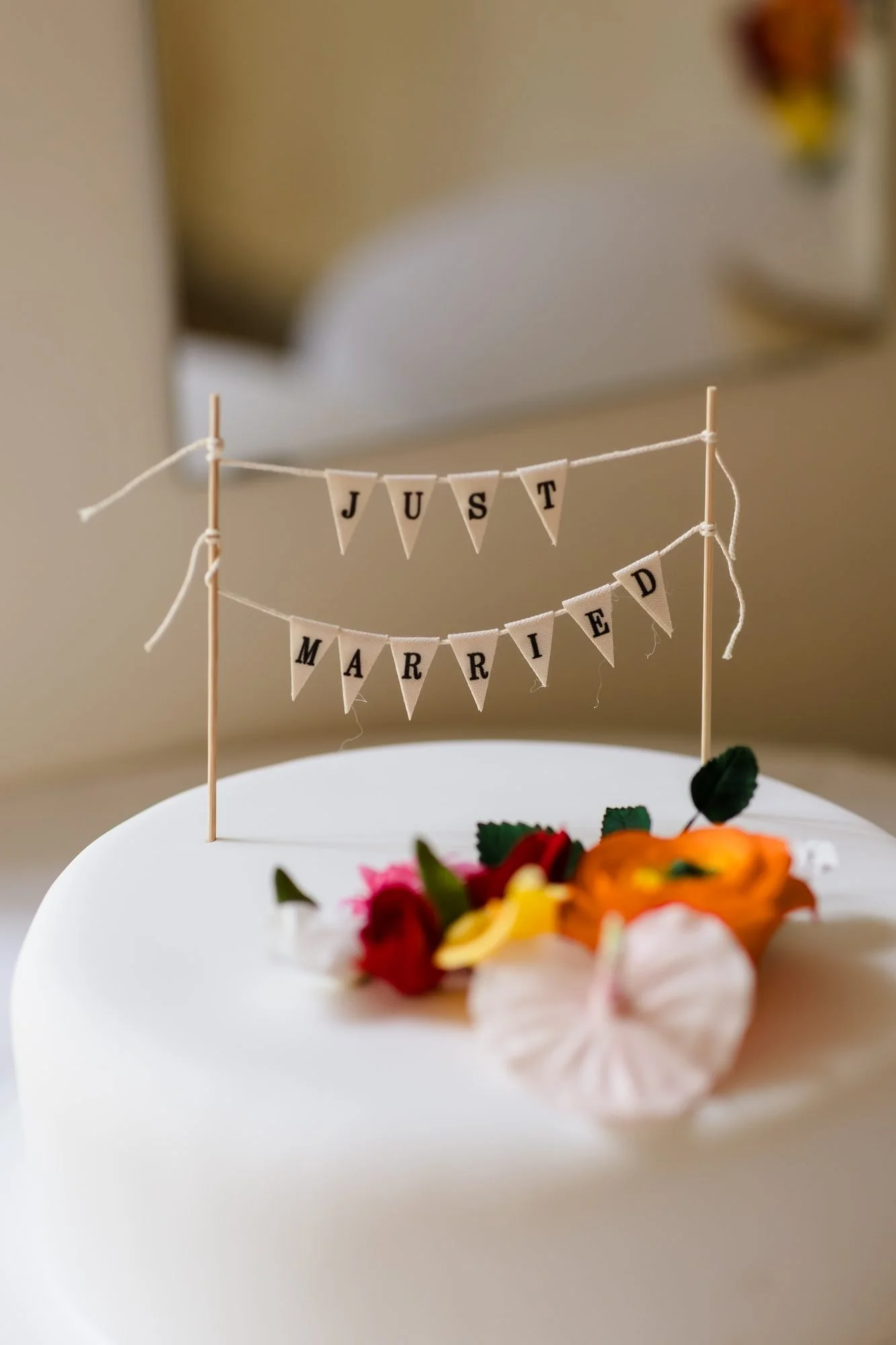 Just Married bunting cake topper and tropical flowers on a white iced wedding cake at Warwick House
