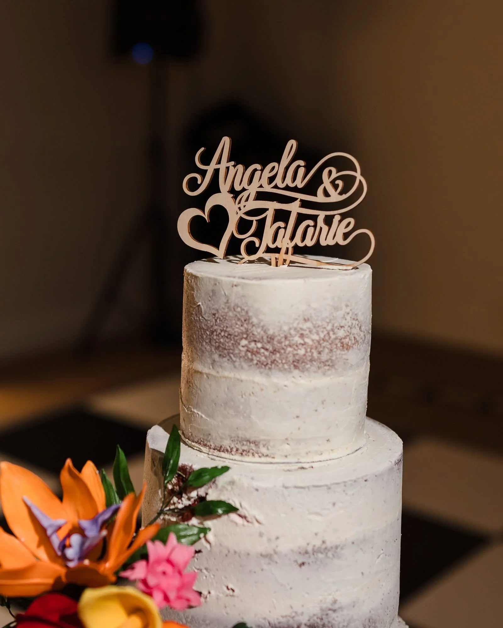 Semi-naked wedding cake with an Angela and Tafarie name topper and tropical flowers at Warwick House