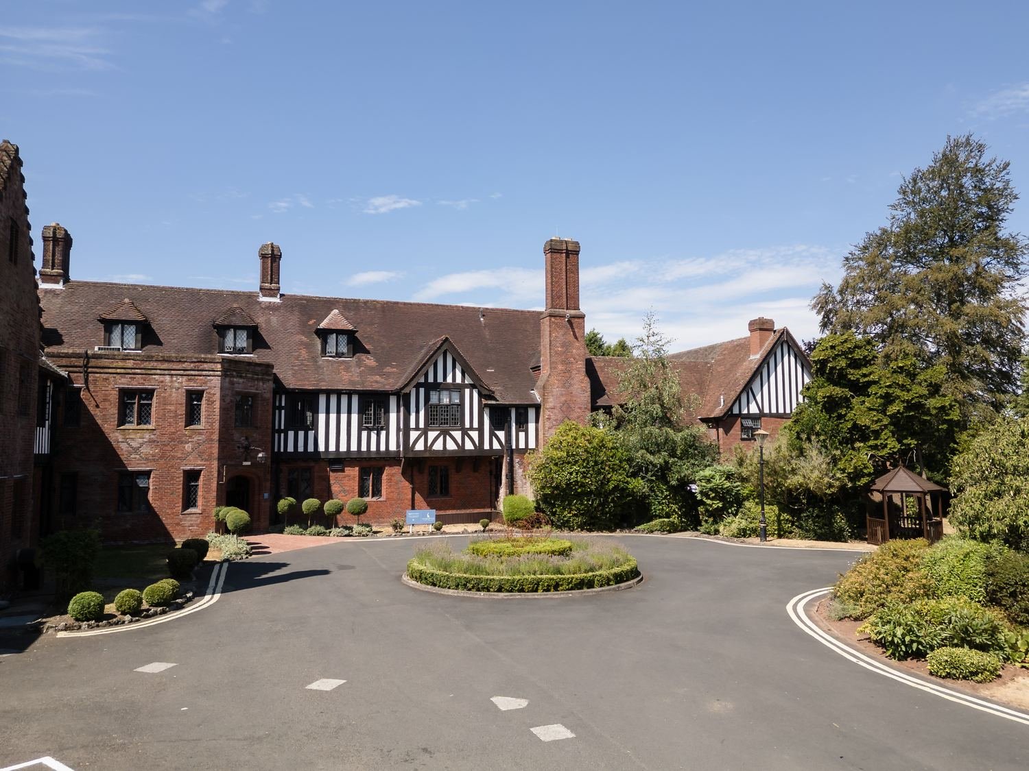 The Tudor-style brick and timber frontage of Hogarths Stone Manor with its turning circle and clipped topiary under blue skies