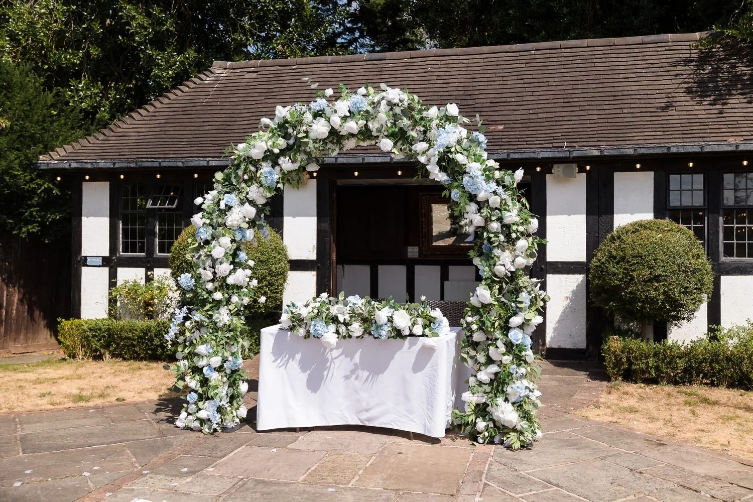 Floral arch of white roses and pale blue hydrangeas over the white-clothed ceremony table outside the Pump Rooms