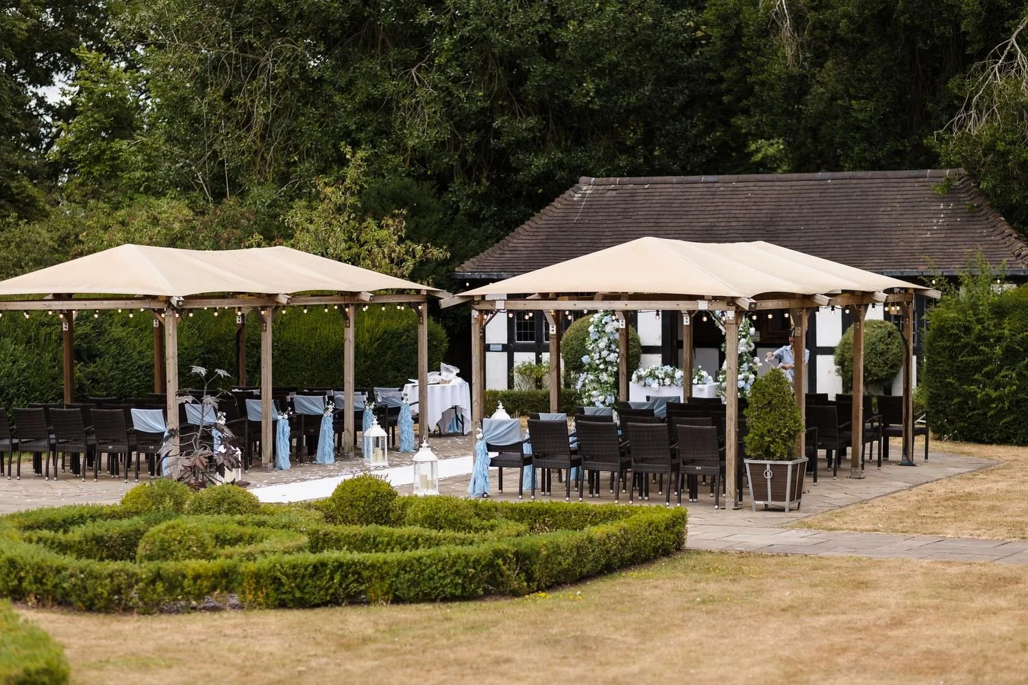 Wide view of the ceremony canopies, rattan chairs and knot garden in front of the black-and-white Pump Rooms building