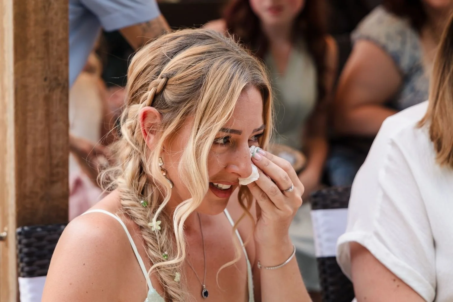 A guest with braided blonde hair wiping away a happy tear with a tissue during the ceremony