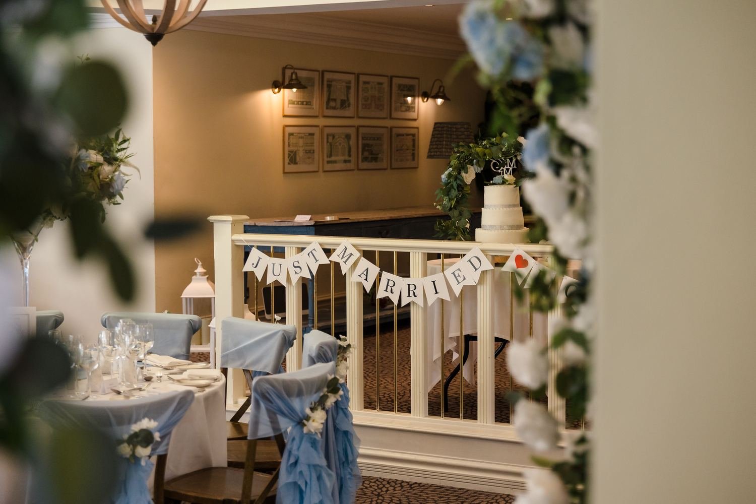 Just Married bunting on a white balustrade with the wedding cake beyond, seen through soft flowers in the foreground