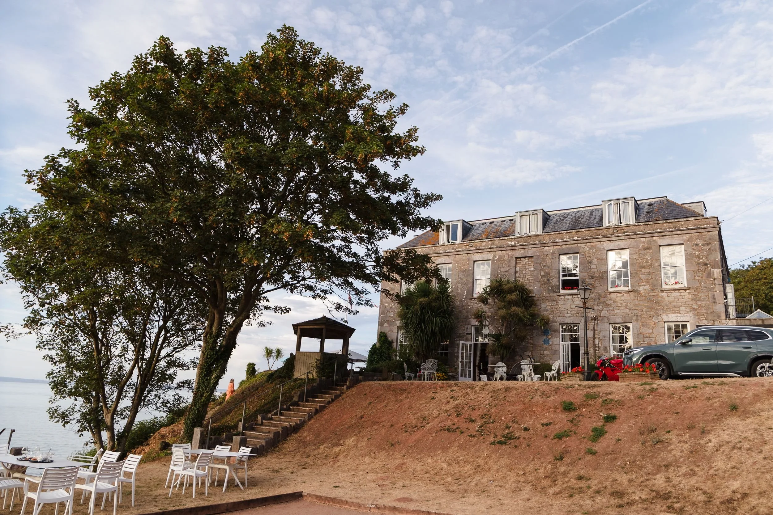 Stone exterior of Berry Head Hotel in Brixham, with steps leading down to the sea-view lawn in evening light