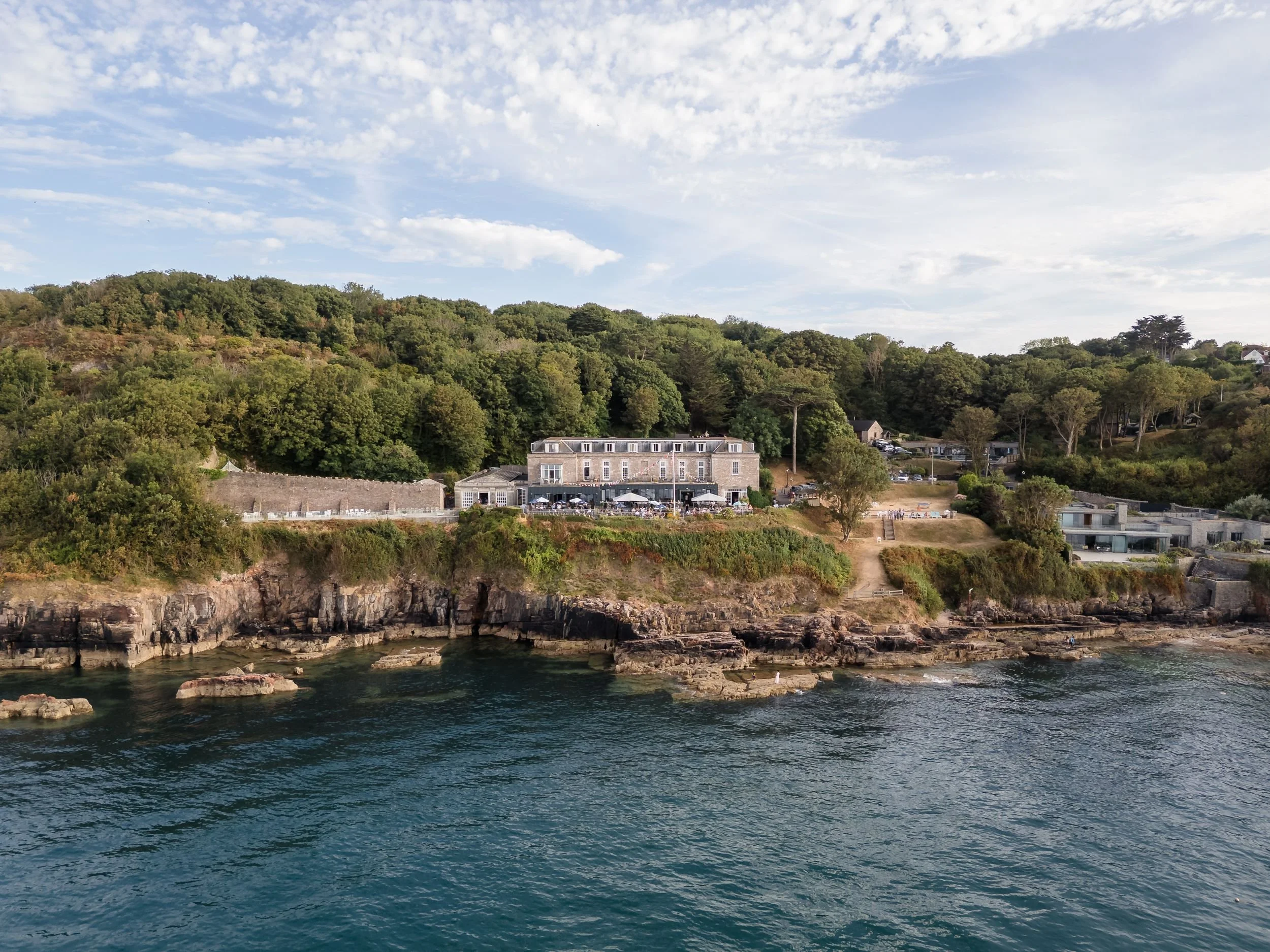 Drone photograph of Berry Head Hotel from the sea, showing the deck, the cliffs and the rocks below