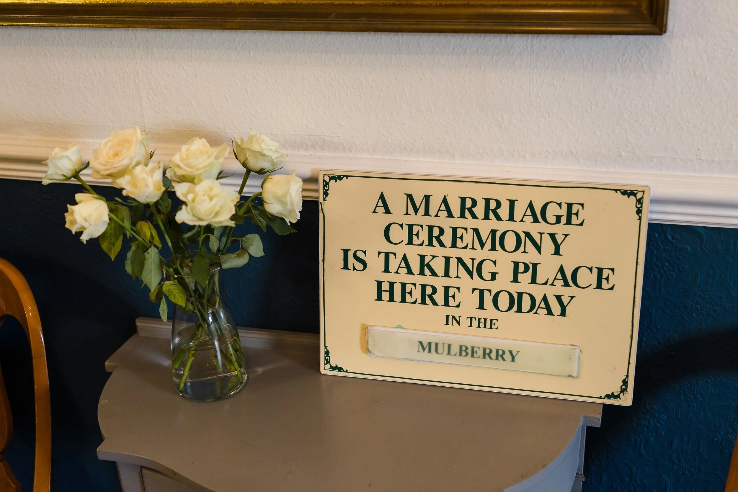 Sign reading A marriage ceremony is taking place here today in the Mulberry, beside a vase of white roses