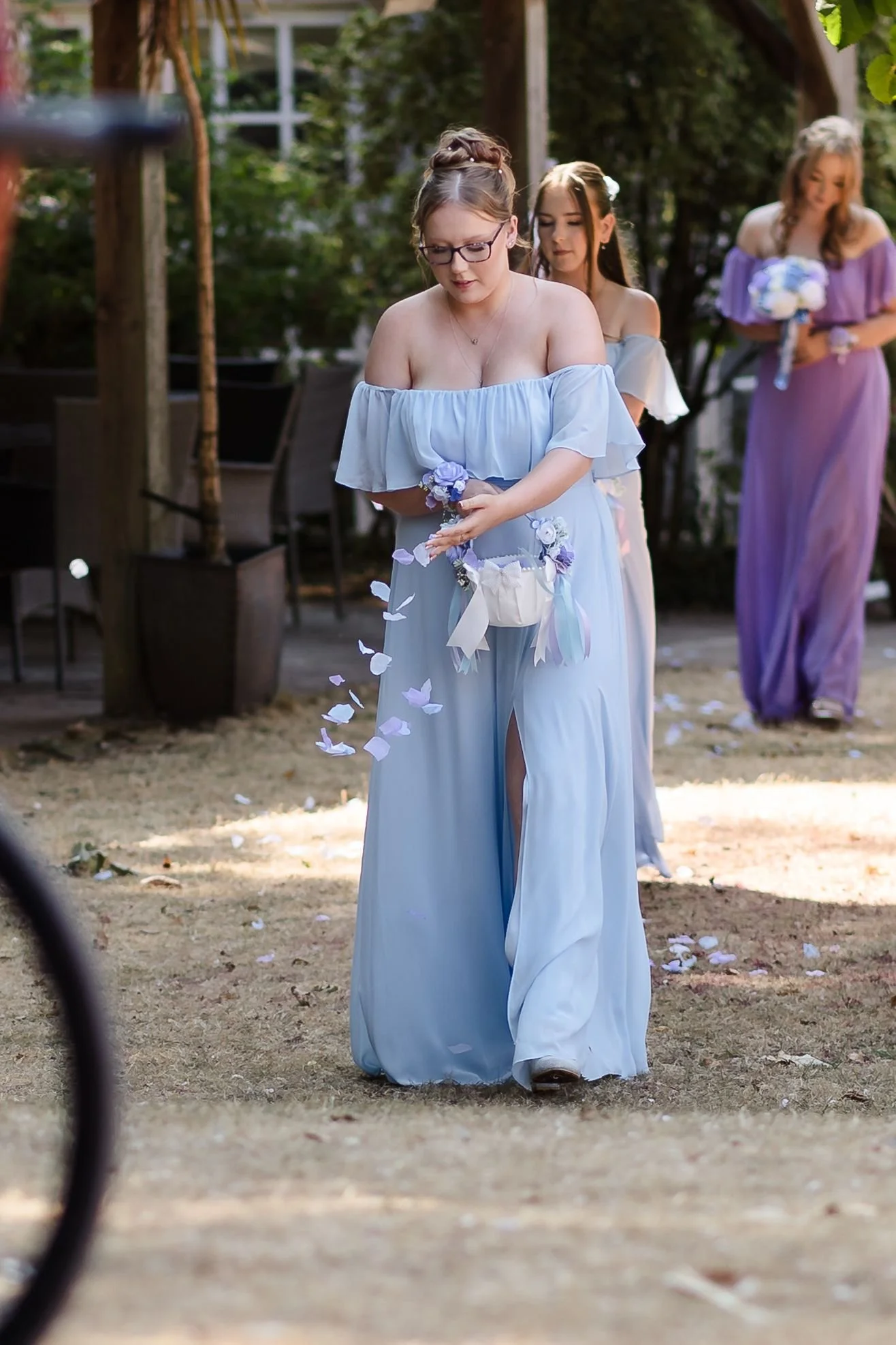 Bridesmaid in a pale blue dress scatters petals along the aisle in the walled garden at Berry Head Hotel