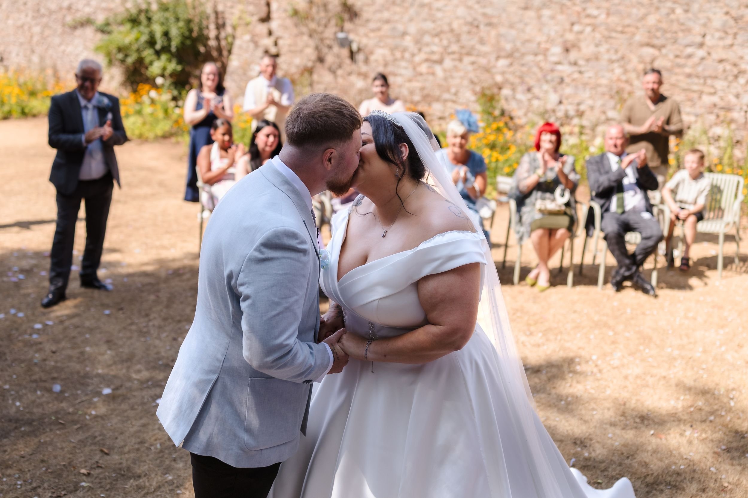 Bride and groom share their first kiss as guests applaud in the walled garden at Berry Head Hotel