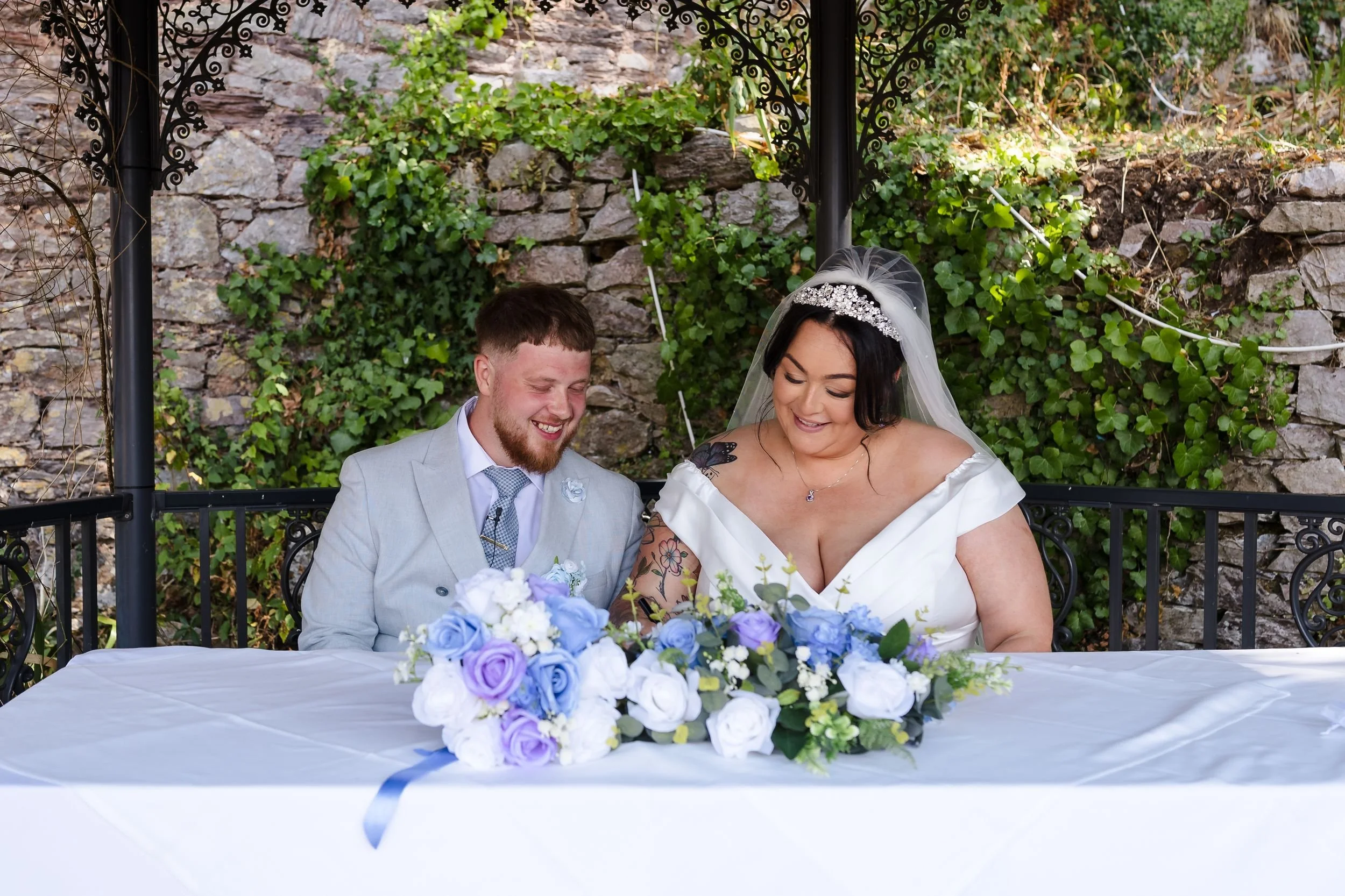 Bride and groom laugh while signing the register under the gazebo in the walled garden at Berry Head Hotel