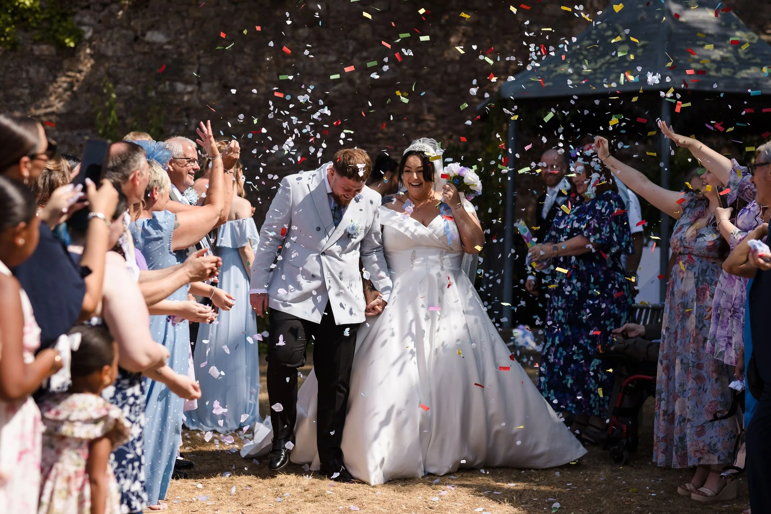 Guests throw colourful confetti over the bride and groom in the walled garden at Berry Head Hotel