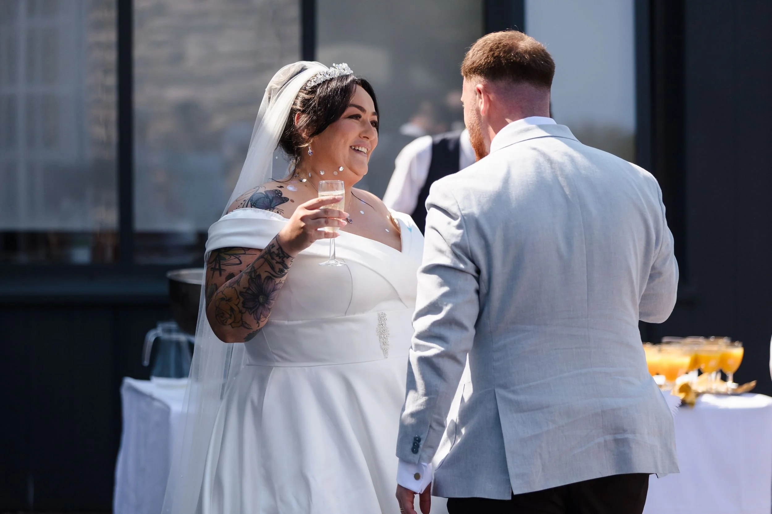 Bride holding a glass of fizz smiles at the groom during the drinks reception on the deck at Berry Head Hotel