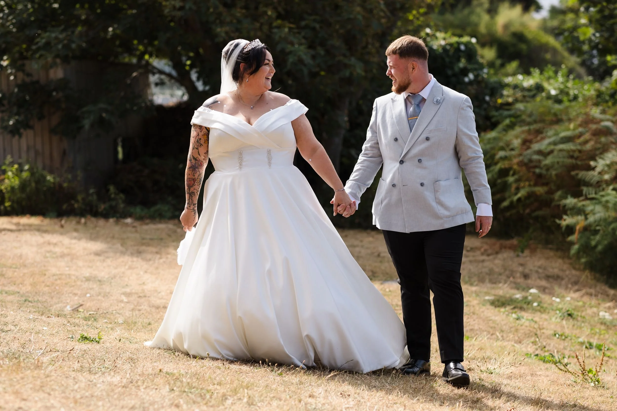 Bride and groom walk hand in hand across the lawn at Berry Head Hotel, laughing together