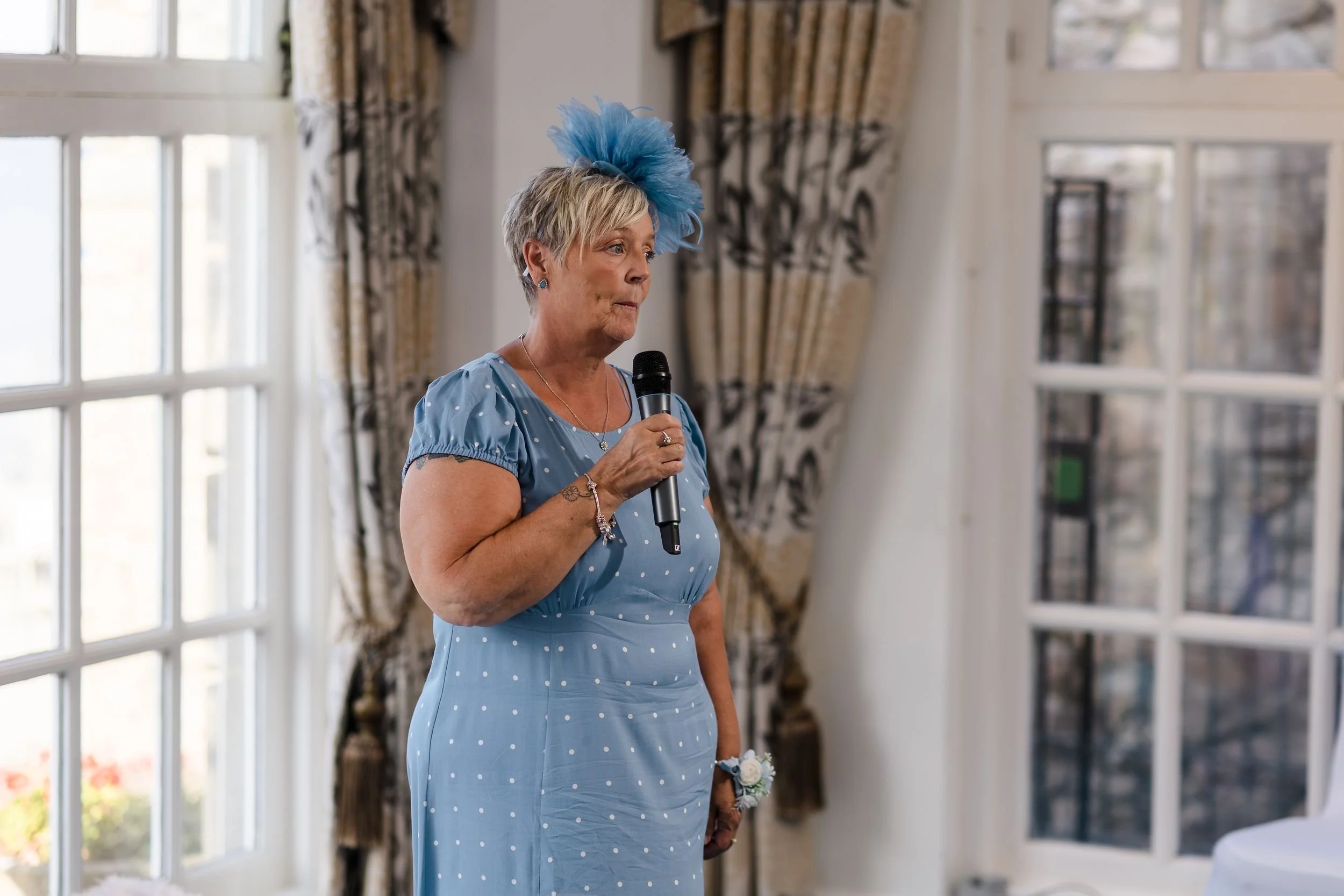 Wedding guest in a blue dress and feather fascinator gives a speech in the Mulberry Room at Berry Head Hotel