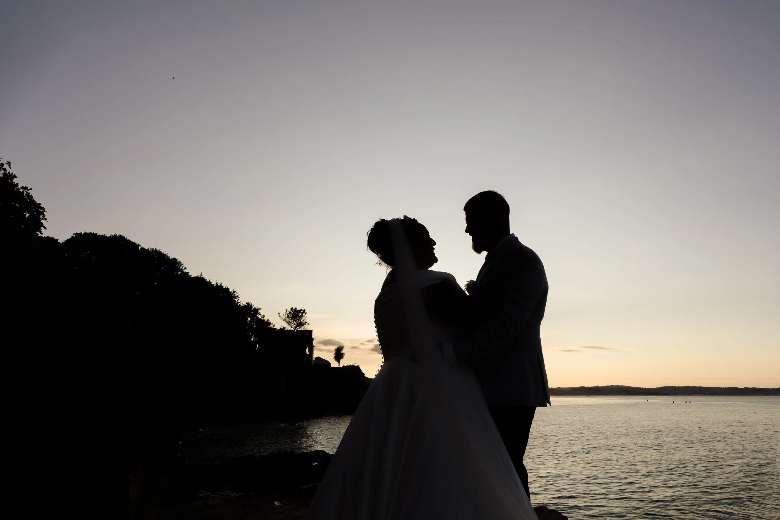 Silhouette of the bride and groom on the rocks at Berry Head, Brixham, against the sky at dusk