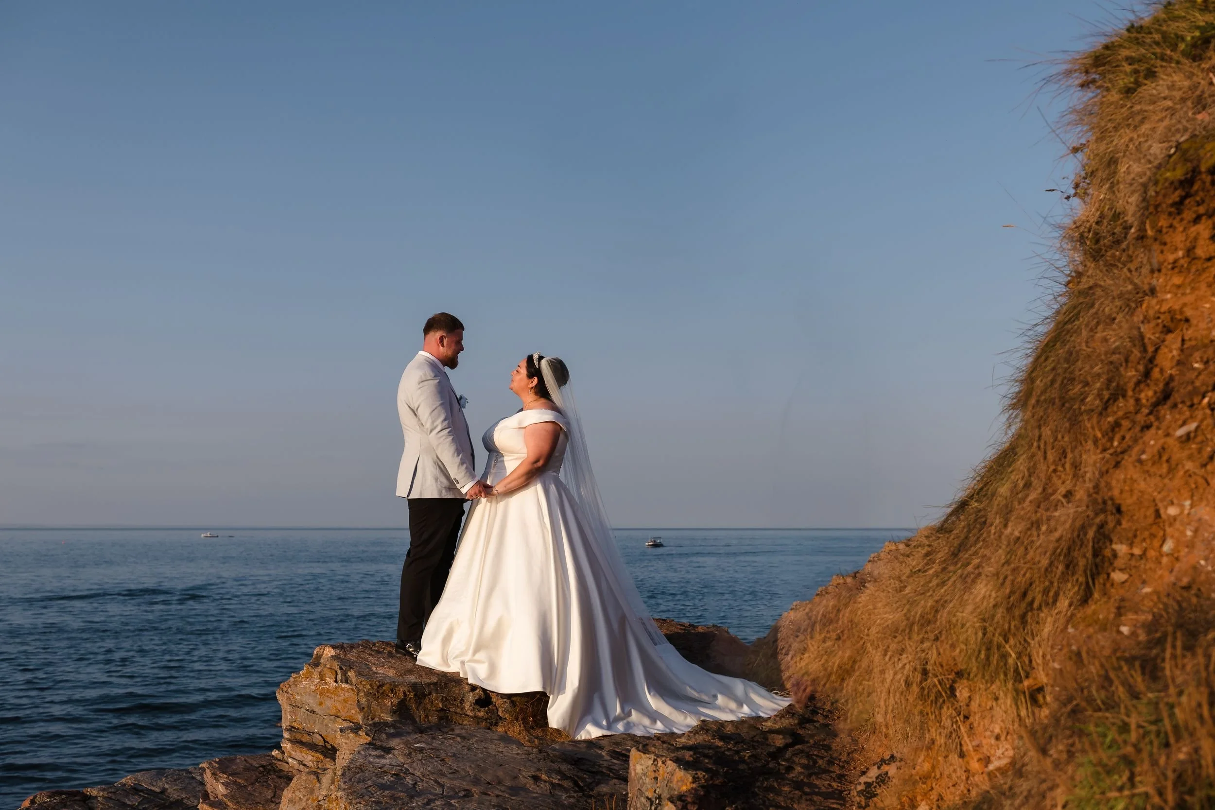 Bride and groom on the rocks below Berry Head Hotel, Brixham, lit with off-camera flash against the evening sky