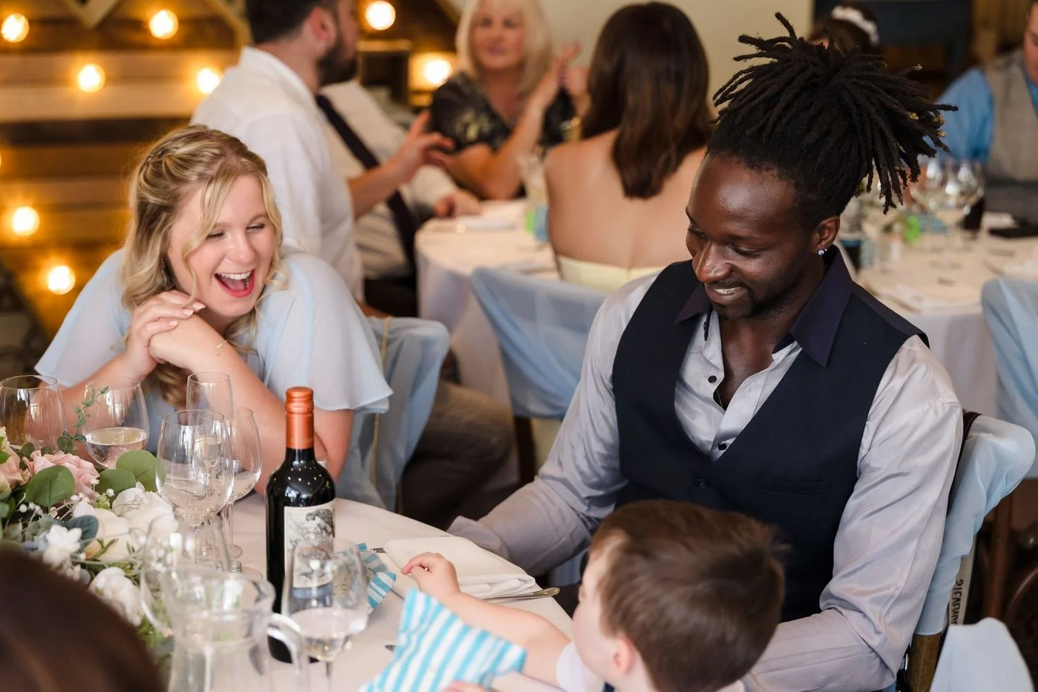 Guests laughing together around a table during the wedding breakfast in the Garden Room