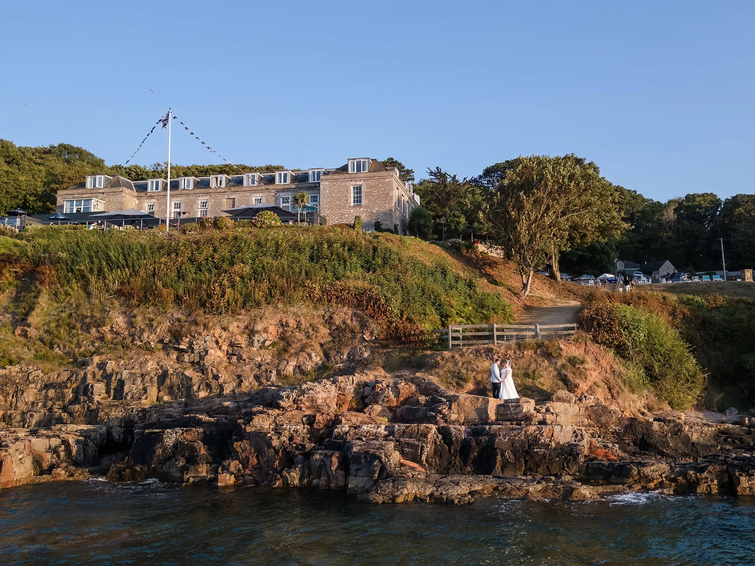 Drone photograph of a bride and groom on the rocks below Berry Head Hotel in Brixham, taken from the sea