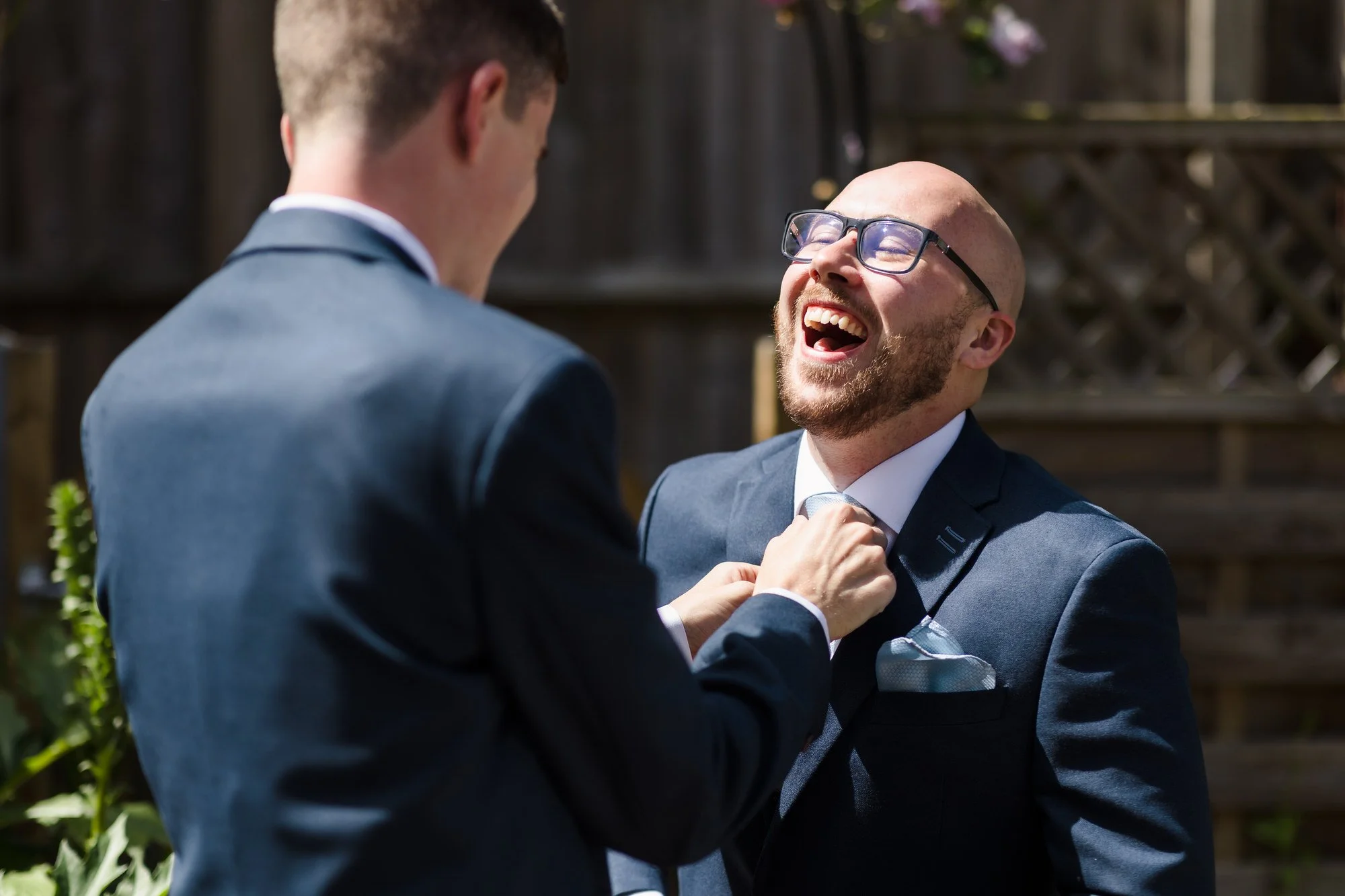 Groom laughing as his best man adjusts his tie before the ceremony, candid preparation photography in Worcestershire