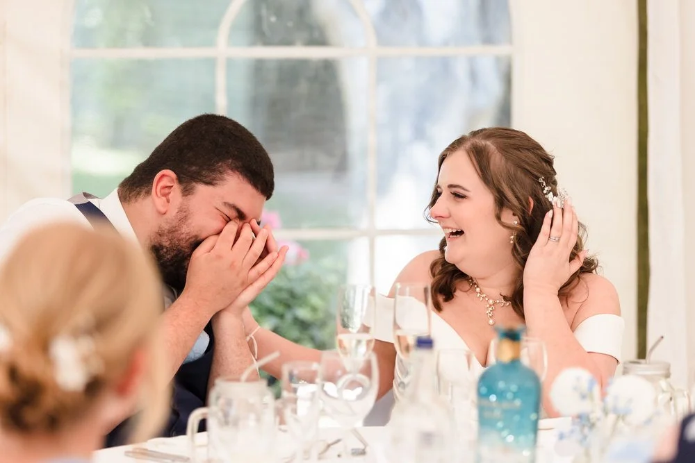 Laughing during speeches at Karma Salford Hall—groom hides his face as the bride smiles at the top table