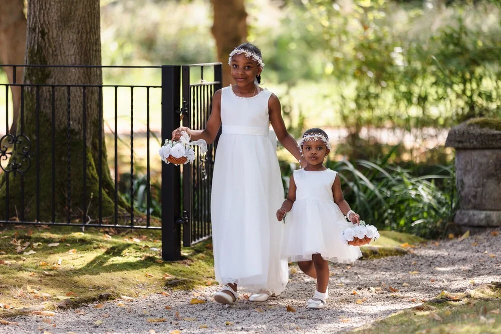 Two flower girls in white dresses walking hand in hand through the iron gate at Hogarths Hotel Solihull.