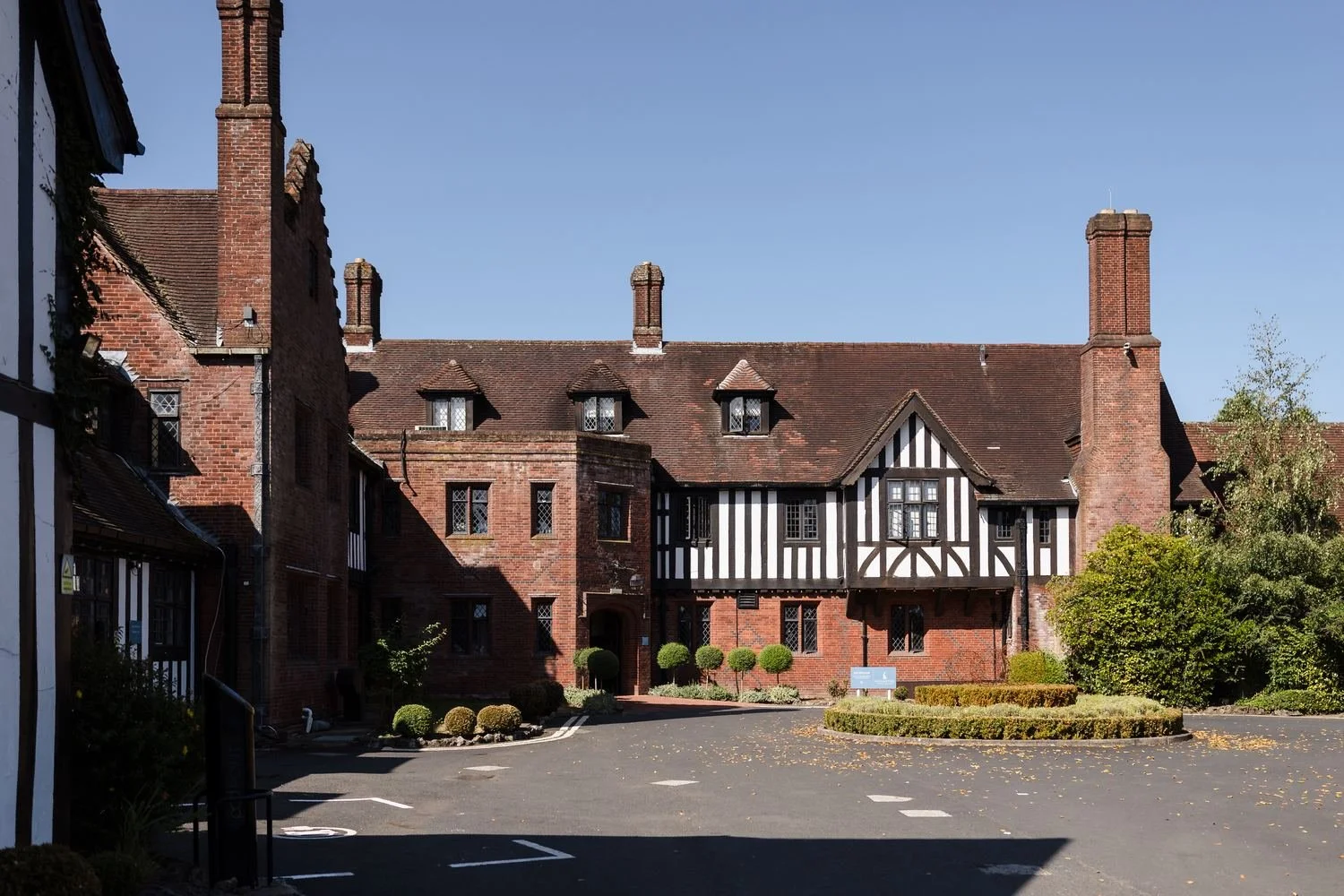 The Tudor-style timber-framed frontage and tall brick chimneys of Hogarths Stone Manor under a blue sky