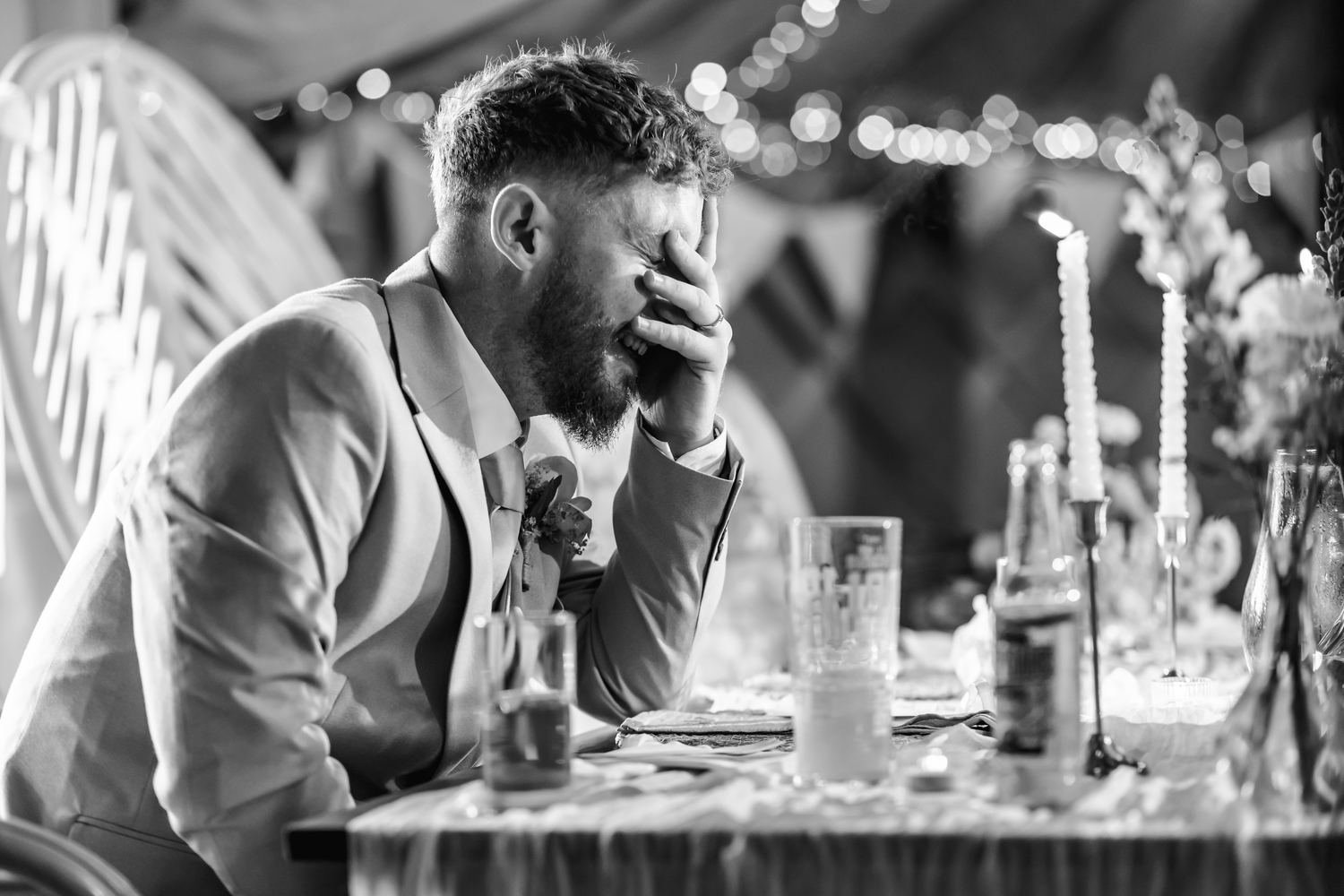 Black and white photograph of Sean laughing with his hand over his face at the top table during the speeches