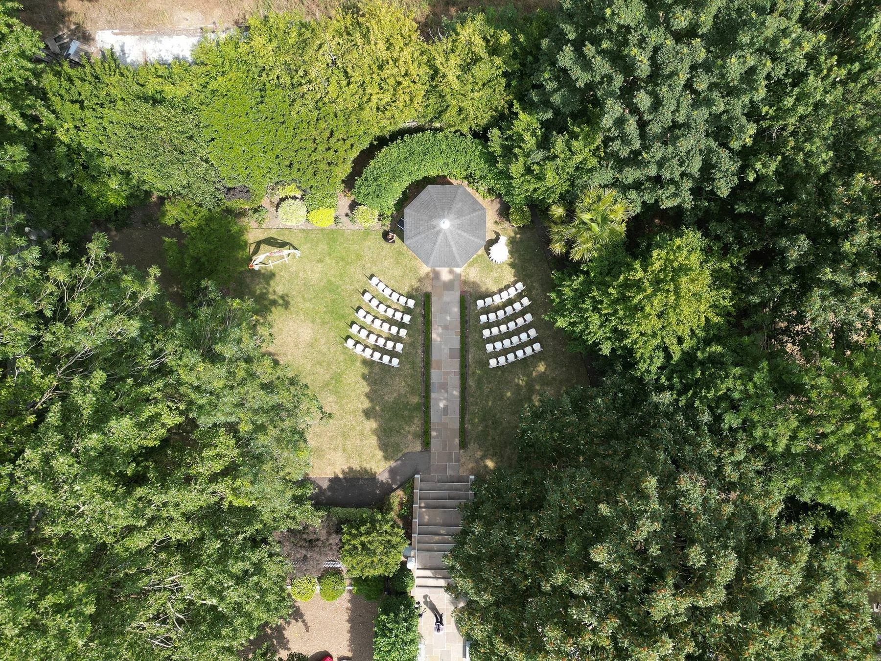 Drone view looking down on the outdoor ceremony garden at Warwick House, with the gazebo, aisle and chairs set out