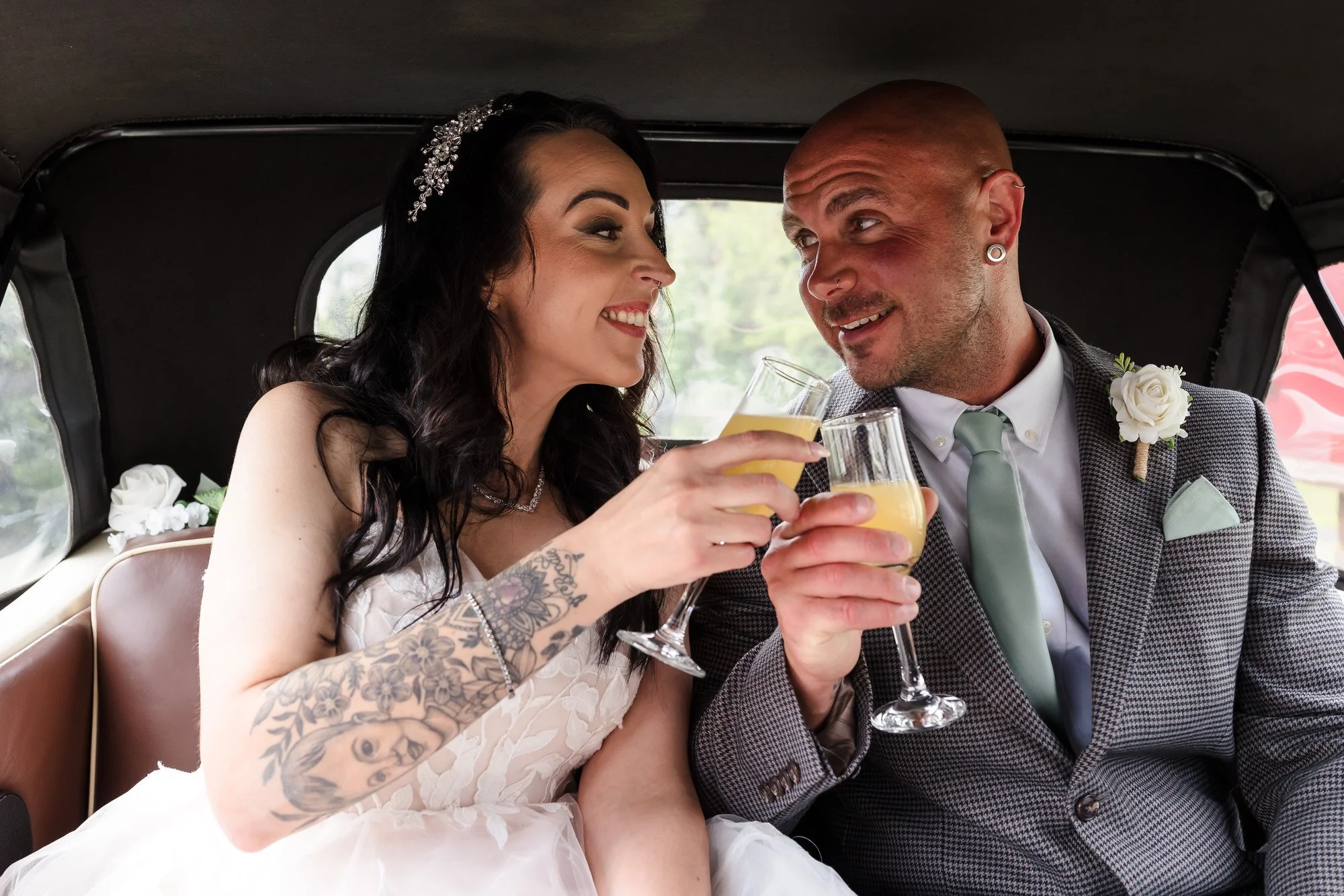 Bride and groom toasting with drinks in the back of their vintage wedding car after the ceremony.
