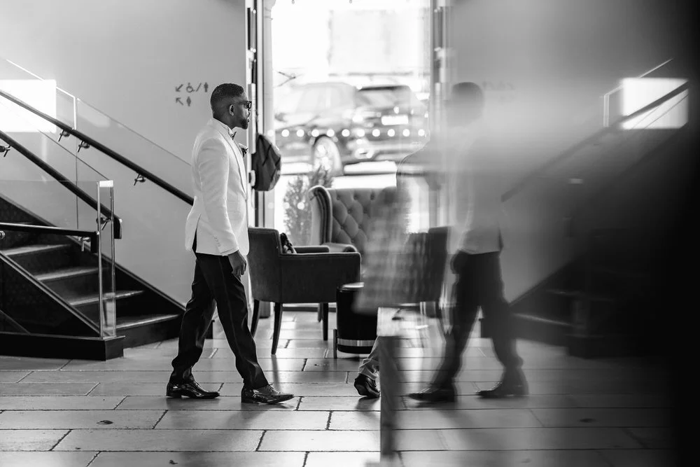 Documentary black-and-white photograph of the groom walking through the Hogarths Solihull hotel lobby before the ceremony.