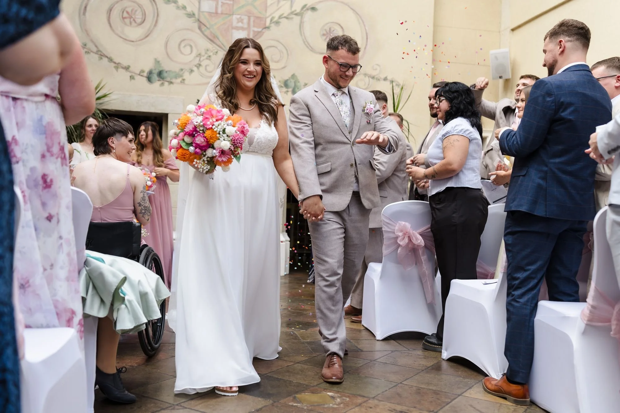Holly and Dan walking hand in hand back down the aisle as guests throw confetti in the ceremony room