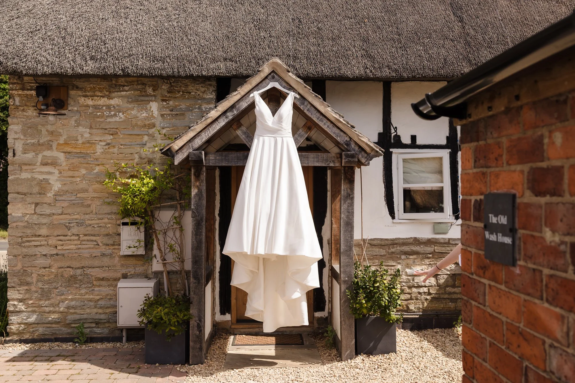 Wedding dress hanging in a thatched cottage porch before the ceremony, bridal preparation photography in Worcestershire